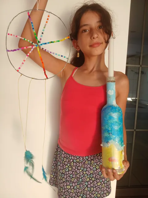 Girl displaying her candle holder alongside a colourful beaded dreamcatcher