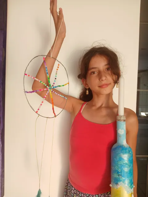 Girl presenting two finished Art Club creations: a candle holder and dreamcatcher