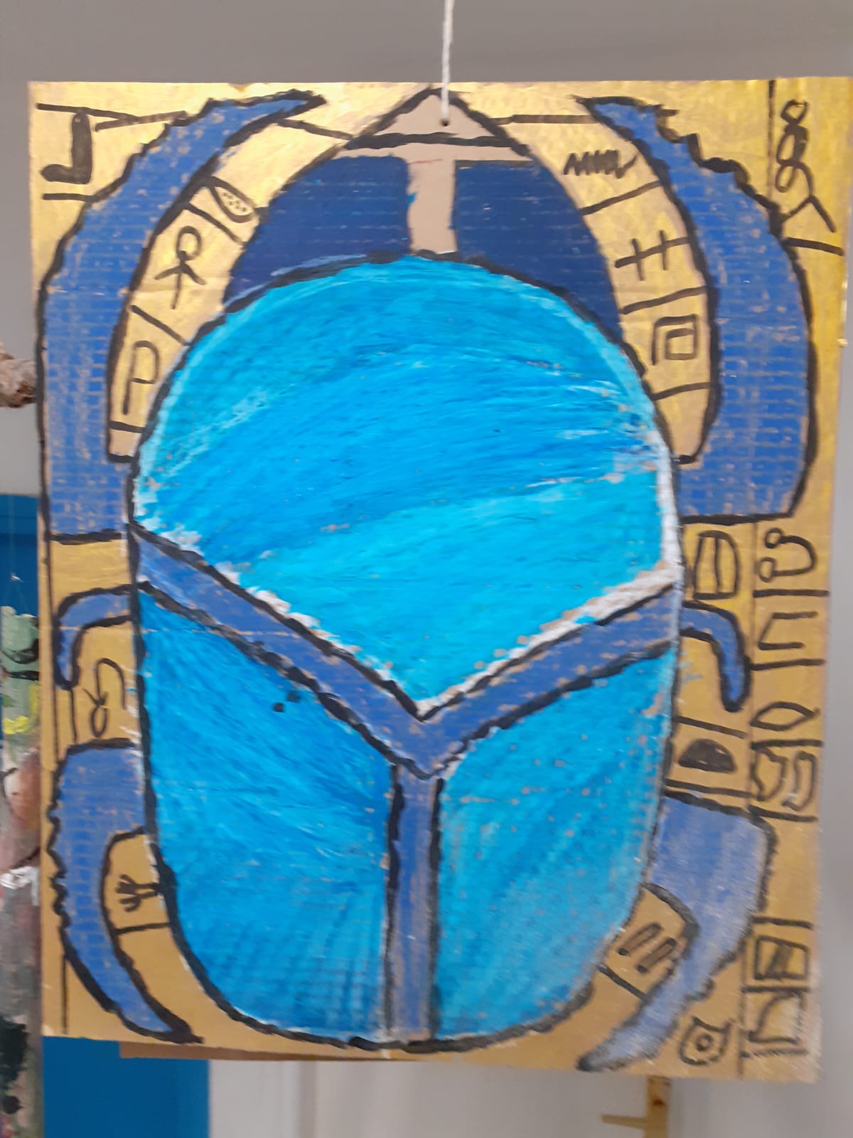 Blue scarab artwork on cardboard with gold hieroglyph-style markings