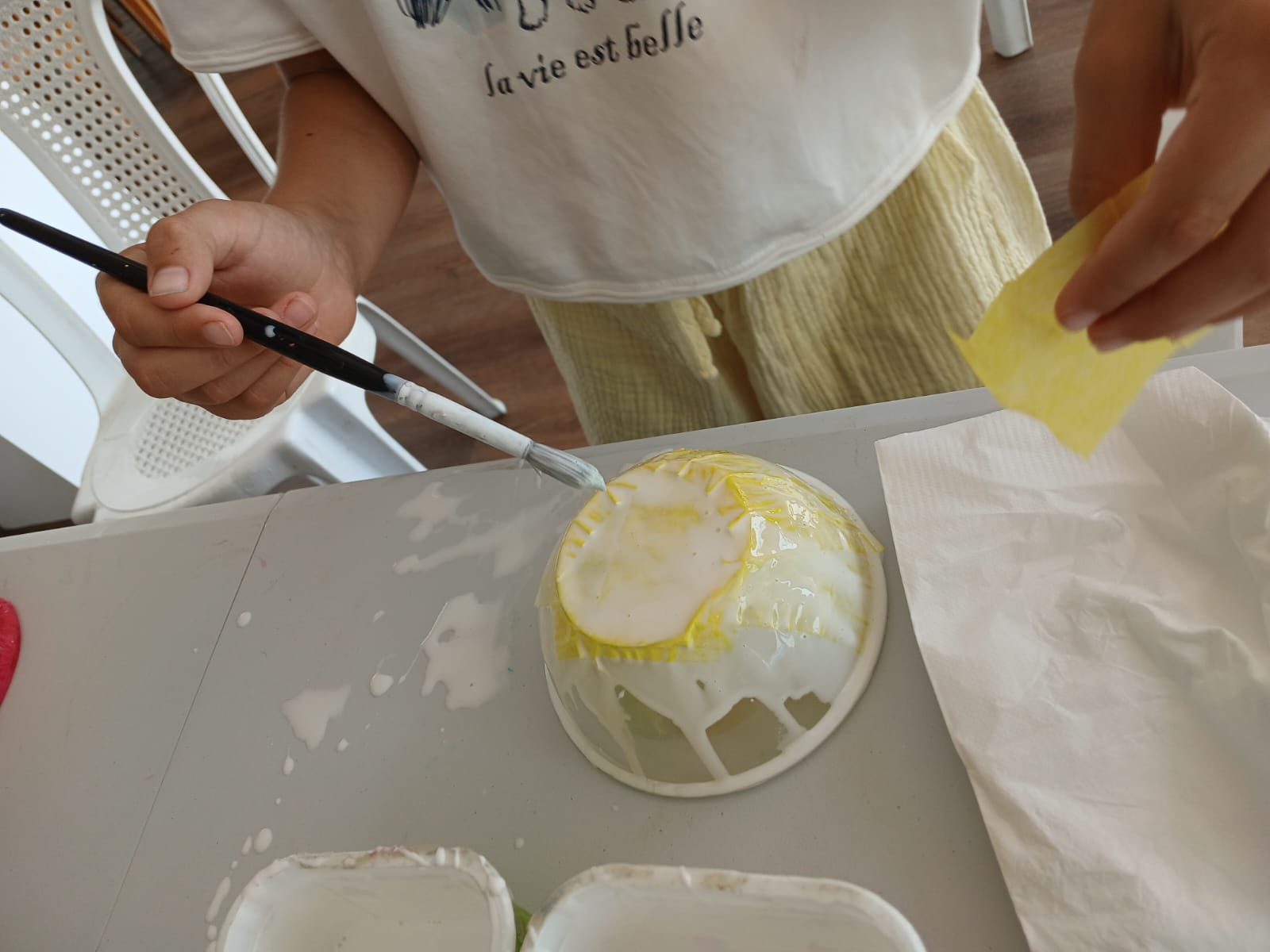 Child brushing glue onto a yellow paper bowl craft