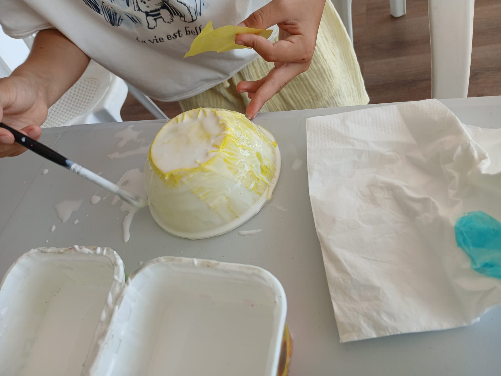 Paper bowl craft being covered with yellow tissue paper